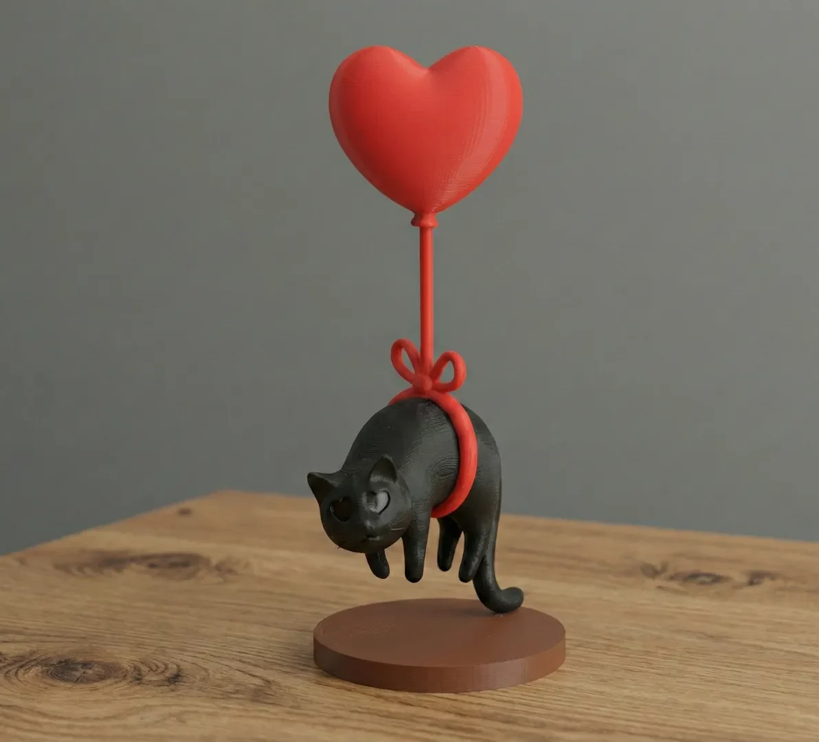 Black cat figurine floating from a red heart-shaped balloon on a round base