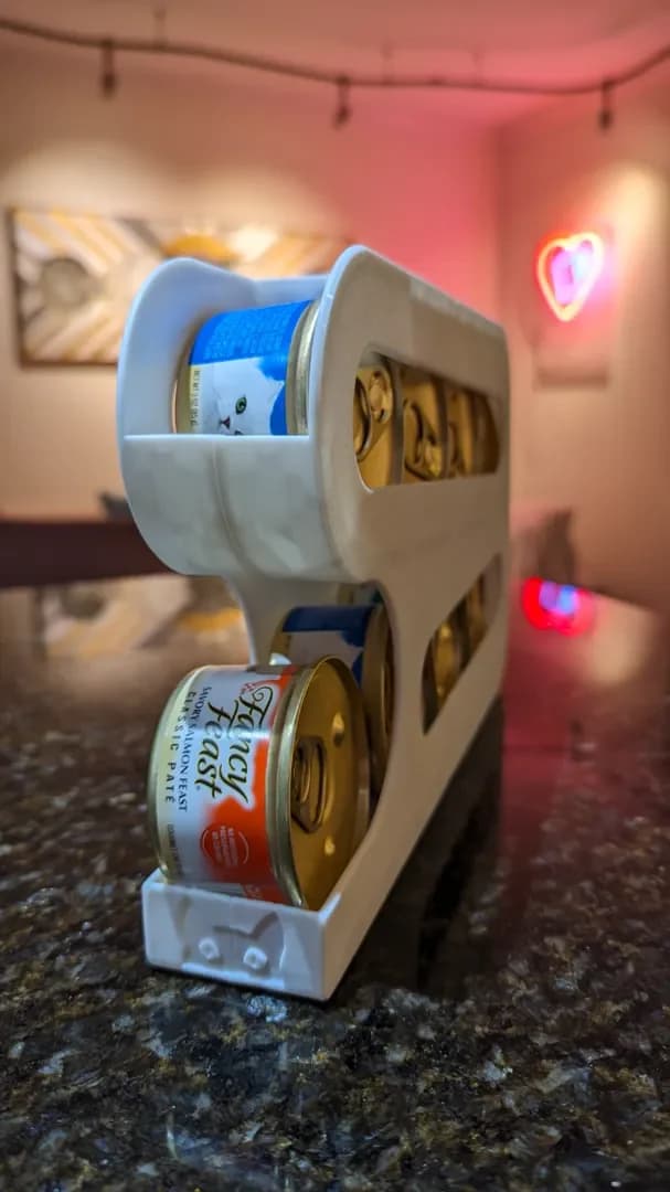 White cat food can dispenser holding stacked tins on a kitchen counter