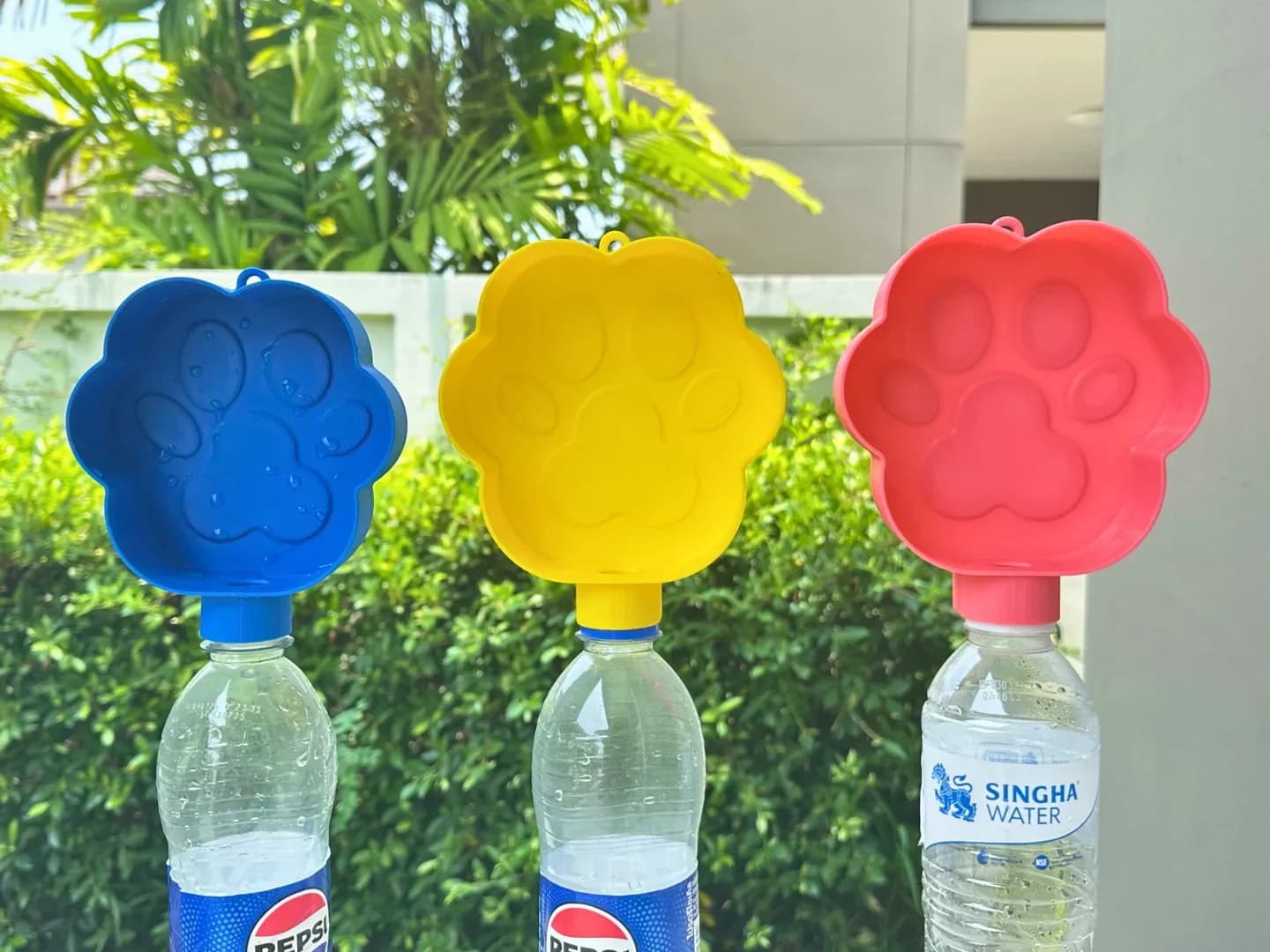 Blue, yellow and red paw-print water bowls attached to upturned bottles